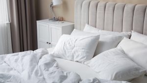 White pillows and clean linens on a bed near a beige wall — the surface most parents worry about after a lice diagnosis.
