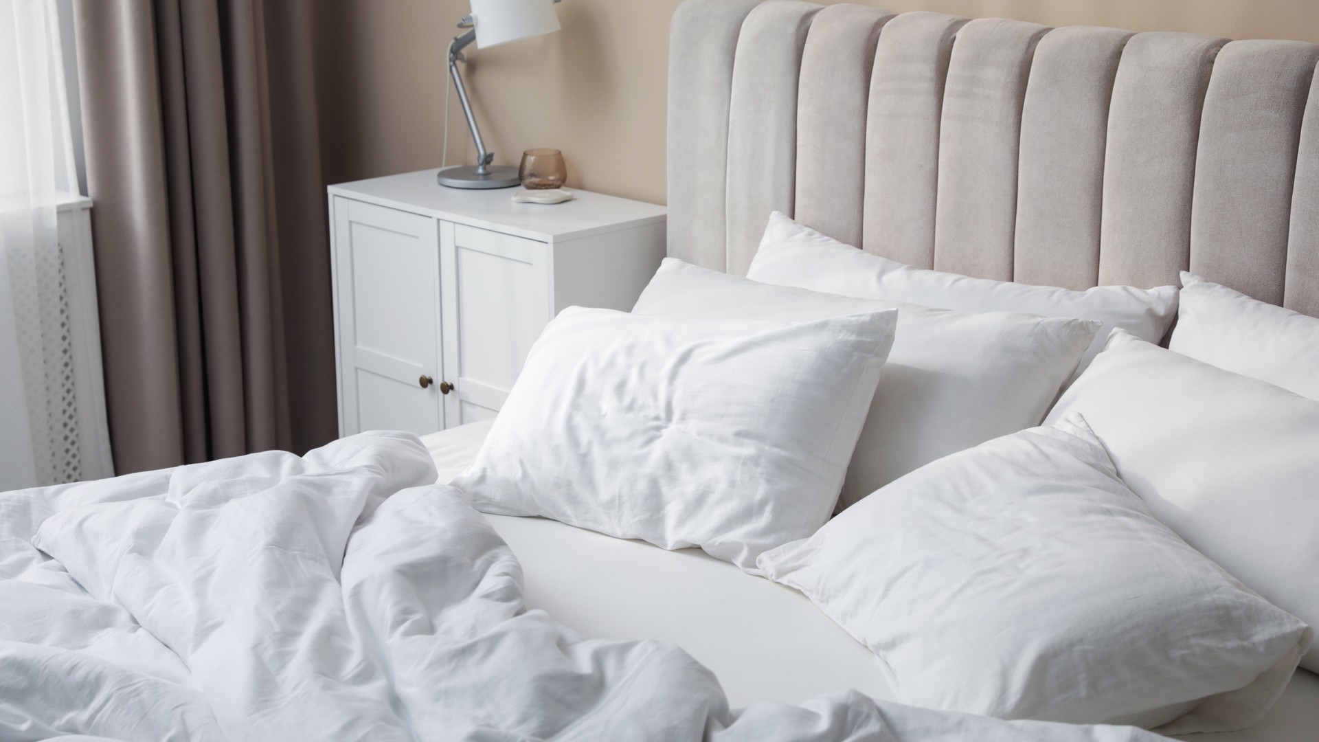 White pillows and clean linens on a bed near a beige wall — the surface most parents worry about after a lice diagnosis.