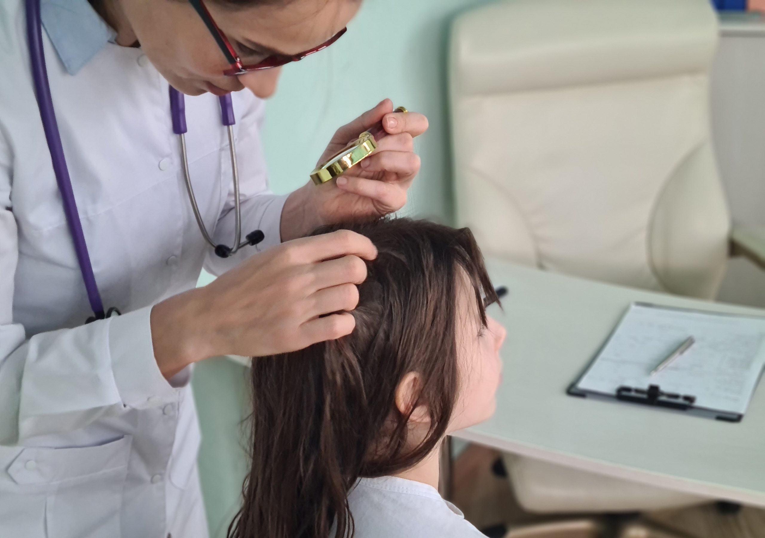 A clinician uses a magnifying glass to examine a child's scalp and hairline closely, confirming whether a single louse or nit is really an active case.