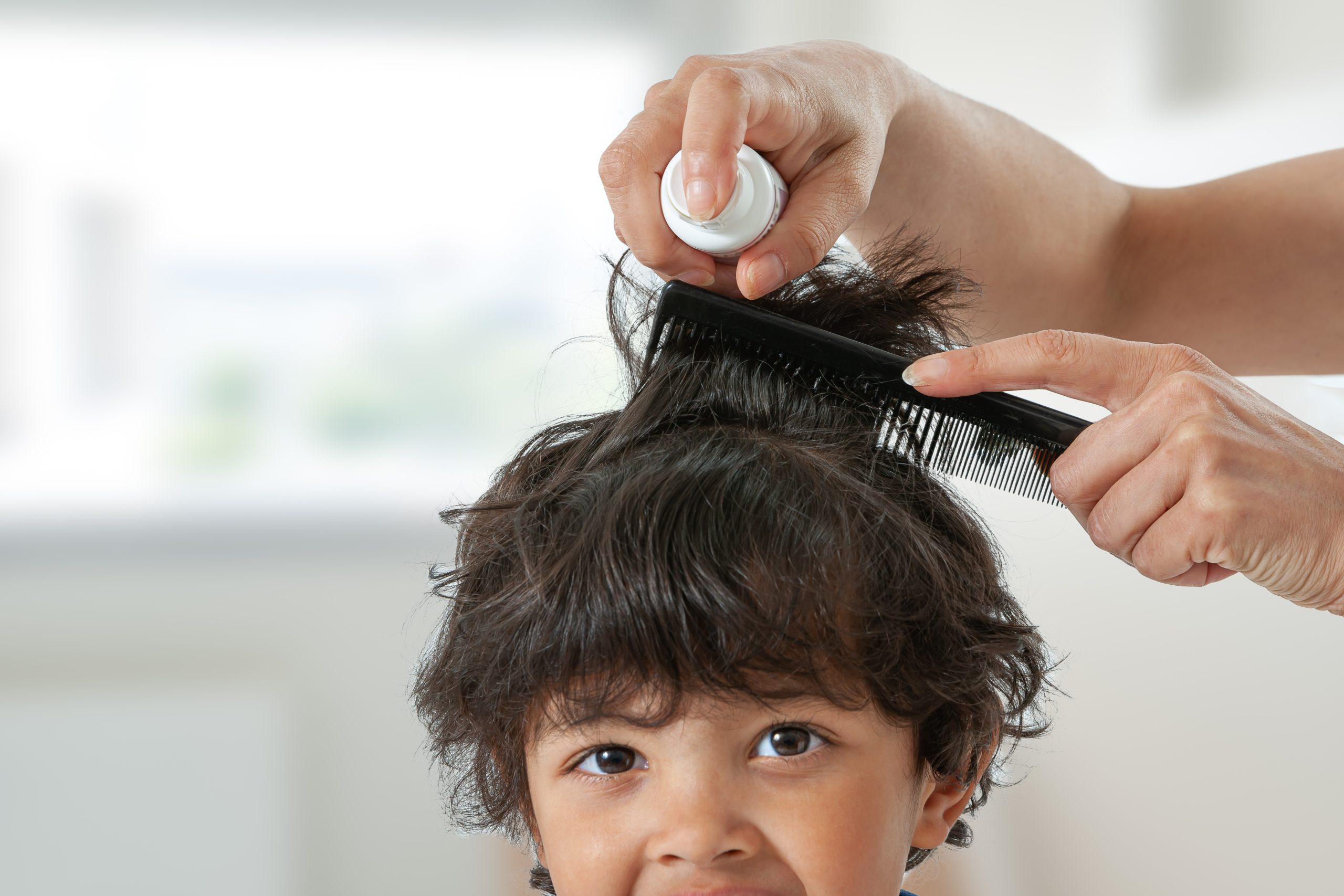 A parent carefully treats and combs through a school-age child's damp hair to remove head lice and eggs, finishing the hands-on step that makes lice removal last.
