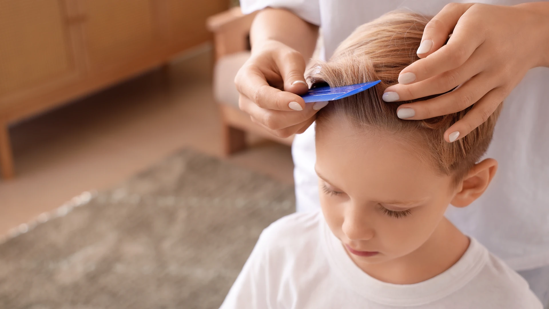 Hands separate short light hair with a small blue comb near the hairline.